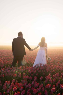 A bride and groom holding hands while walking through a tulip field at sunrise in the Netherlands, captured as a romantic wedding moment by Vidora Studio.