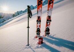 A can of Dr Pepper Zero Sugar rests in the deep snow at the base of a pair of skis, with a ski pole nearby, on a sunlit, snow-covered mountainside.